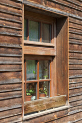 Window in the wooden wall of a beautiful house. There are flowers on the windowsill