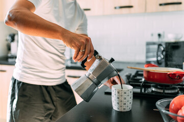 The man's hand holds an antique coffee pot and pours coffee into a white breakfast cup.