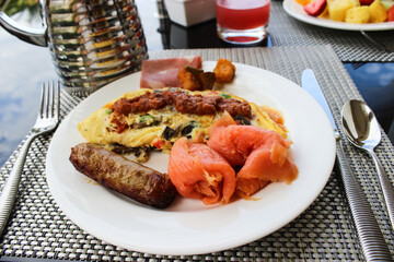 This is breakfast at a five star hotel. Salmon, sausage, egg omelet are on a plate on the table....