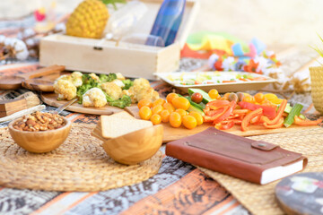Beautiful summer picnic on the beach at sunset. Eco friendly idea for weekend staycations. Organic fresh fruit, vegetables, granola in wood bowls on linen blanket. Selective focus on vegetables.