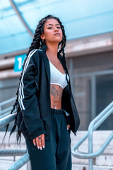 Obraz premium Urban session to trap dancer, with a young brunette of Latin ethnicity with braids, with unbuttoned black sweatshirt and a white top