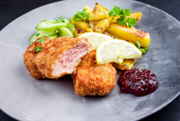 Traditionelles frittiertes Wiener Schnitzel von Kalb mit Bratkartoffel und Gurkensalat angeboten als closeup auf einem Modern Design Teller