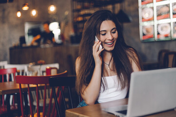 Business woman talking to the phone, working on a laptop and drinking coffee in a cafe.