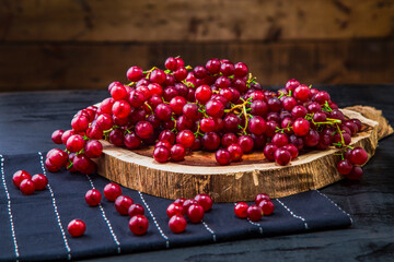 Scattered grape berries on wooden slice and table. Red grape berries arranged over wooden board on table with table runner and wooden background.