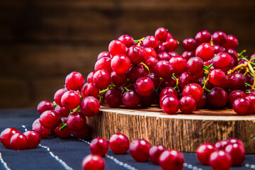Red grape berries arranged over wooden board. Scattered grape berries on wooden slice and table runner with wooden background.