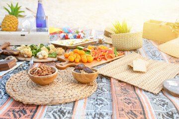 Beautiful summer picnic on the beach at sunset in zero waste style. Organic fresh fruit, cheese and vegetables on linen blanket. Eco friendly idea for weekend staycations. - obrazy, fototapety, plakaty