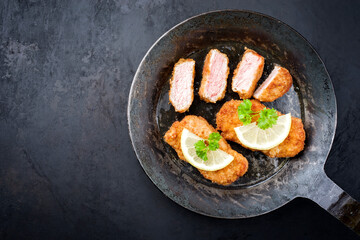 Traditionelle frittierte Kalbssteaks mit Zitronenscheibe und Kräuter angeboten als Draufsicht in einer rustikalen schmiedeeisernen Pfanne mit Textfreiraum links 