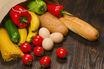 Food in a paper bag on a wooden background. Long loaf, bread, spaghetti, cucumber, peppers, eggs, and bananas, grocery bag