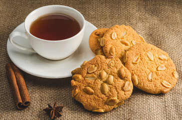 Cookies with peanuts and black tea in a white cup on a saucer, anise star and cinnamon stick. Retro style dinner