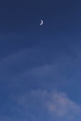 Vertical skyscape, blue sky with soft cluods and a crescent white and shining moon.