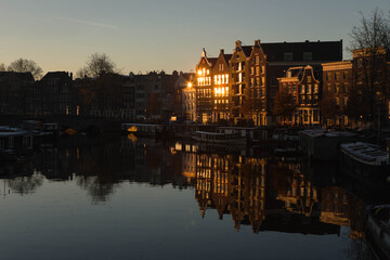 characteristic Dutch houses illuminated by the sun rising along the waalseilandgracht canal (Nieuwmarkt en Lastage district), closed to central station in Amsterdam city, Netherlands, Holland, Europe.