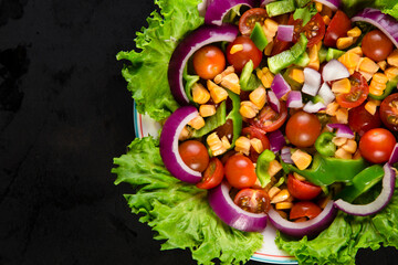 Top view of plate with salad on black table. Cropped plate with salad of chopped onion, tomatoes, green pepper with lettuce with black background.
