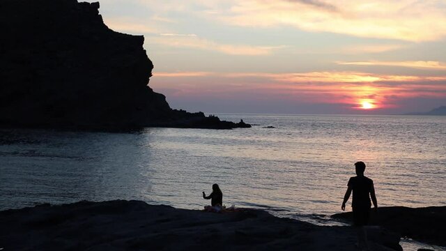 Fascinating island view at sunset with romantic couple 
 silhouette on rocks