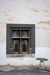 Fototapeta na wymiar Old dark antique window with black round table on the stone pavement .