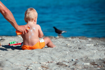 The male hand applies sunscreen to the baby is back.