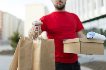 Young handsome deliveryman in red uniform with brown paper package