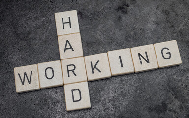 wooden letter tiles forming words on a grey cast iron surface in the background, working hard