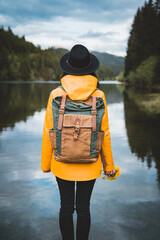 Back view of stylish hipster woman holding flowers,wearing vintage backpack, hat and yellow jacket...