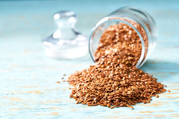 flax seeds are poured from a glass jar on a blue wooden table.