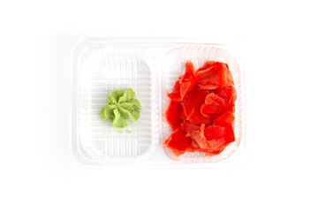 Green wasabi and pink marinated ginger are in plastic container from food delivery service on white background