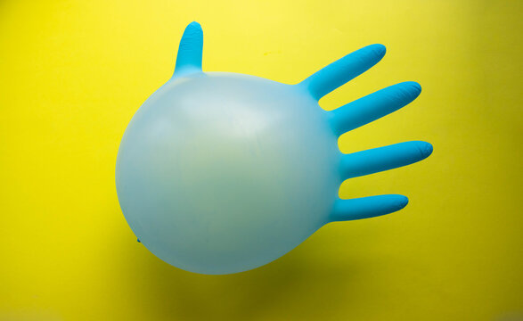 Flying Blue Rubber Surgical Glove In The Form Of A Balloon On A Yellow Background With A Copy Of Space. The Concept Of Minimalism.