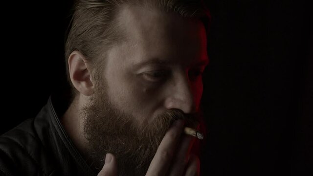 Smoking bearded man on black, close up. Slow motion