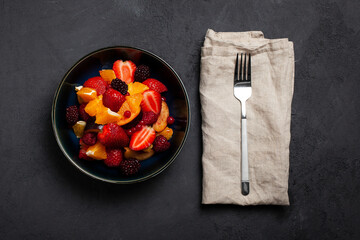 Fresh fruit salad, top view in a bowl on dark concrete background. Vegetarian food concept. Whole food. 