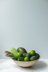 Big plate with different fresh farm green vegetables. Autumn harvest and healthy organic food concept. Wooden plate with green vegetables on white background