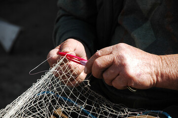 old man is repairing fishing net with hands.