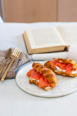Breakfast with croissant, cream cheese and smoked salmon. Old book on the background.