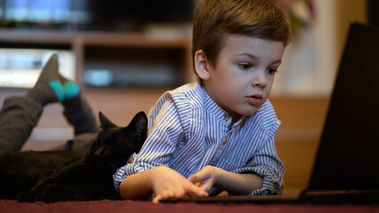 Funny child with kitten using a laptop at home.