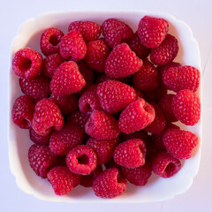 ripe fresh red raspberries in a white plate on a white background