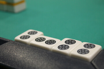 The bones or tiles for the mahjong lie on the green table, the back and side plan is blurred. Table...