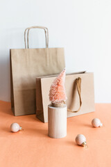 Coconut fiber orange Christmas tree on wooden stand, kraft paper gift bag on pink white background, zero waste festive concept.