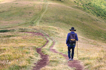 A young man with sombrero, backpack and a walking stick hiking down the hill
