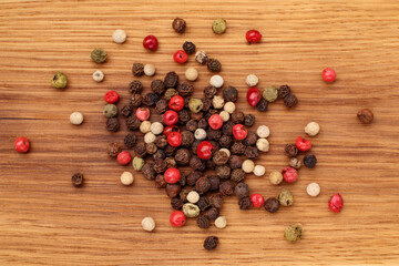 Pile of various peppercorns on wooden board. Mix of black, white, green and red dried peppercorns. Top view.