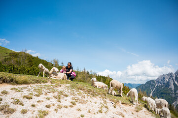 Mother and daughter petting cute sheep in mountain meadow.