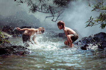 Two boys Happily playing in the water near the stream near their home in the countryside of Thailand