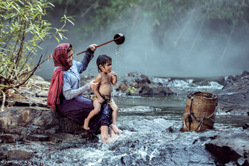 Mother was showering for a baby daughter. At a stream in a rural area of Thailand