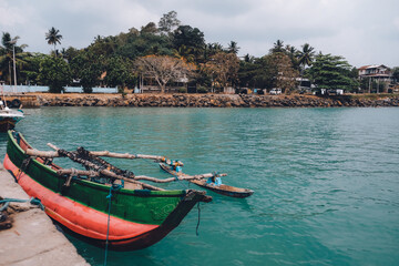 Colorful painted red and green fishing boat tied to the shore. Scenic landscape view from a pier. Local handicraft in Sri Lanka. Blue water. in the sea. Weekend escape from reality to this paradise.