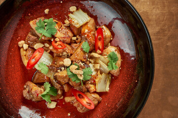 A delicious Asian-style dish, pork in sweet and sour sauce with shiitake mushrooms and hot pepper in a red plate on a metal, copper background. Restaurant serving