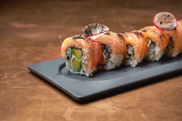Classic japanese sushi rolls - philadelphia rolls with cream cheese, avocado and salmon on a black plate on a copper, metal background
