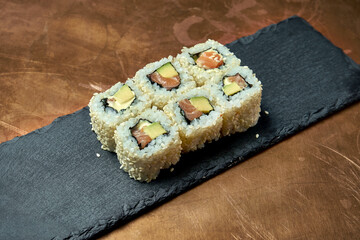 Classic japanese sushi rolls - california rolls with cream cheese, avocado and salmon on a black plate on a copper, metal background