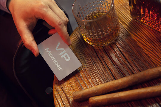 Man's hand puts VIP membership card on the table. Gentleman's hand puts exclusive VIP membership card on the wooden table with whisky in carafe and glass with cigars.