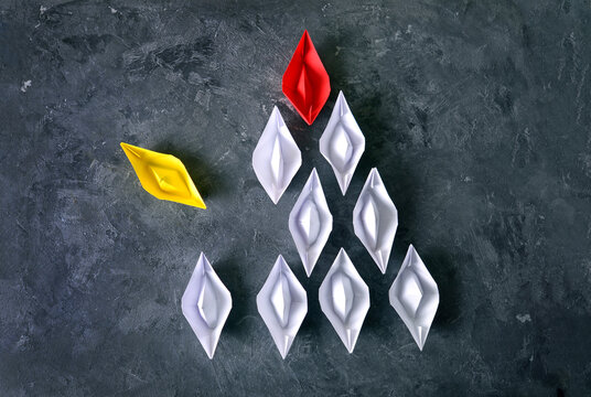 The formation of individuality in society concept with yellow paper boat breaks out from the order of other paper boats with boss.