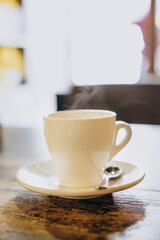 White cup with saucer and small spoon on a wooden table. Hot espresso in a white cup. Delicious coffee for breakfast in a cafe