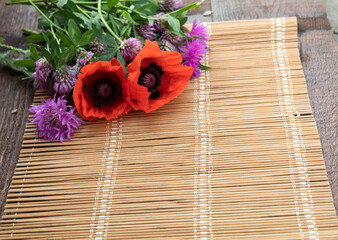 Fototapeta na wymiar Against the background of straw napkins in the corner is a bouquet of poppy flowers, cornflowers and clover.