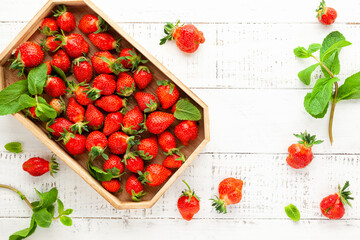 Delicious fresh strawberries in box and leaves of mint on white wooden background, top view.  Flat lay, copy space. Ugly organic strawberry
