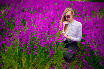 blonde in sunglasses and a white shirt on the field with purple flowers