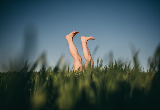 Male legs up, sticking out of the green grass. Walk in the sky. Creative photos, spring.